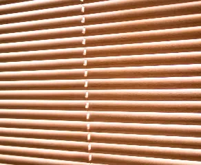 A close-up view of beige window-blinds with thin horizontal slats allowing diffused light to filter through. The gaps between the slats create a pattern of light and shadow across the surface.